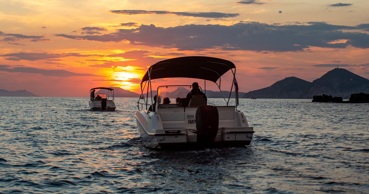 A canopy speedboat on calm water at sunset, with islands behind
