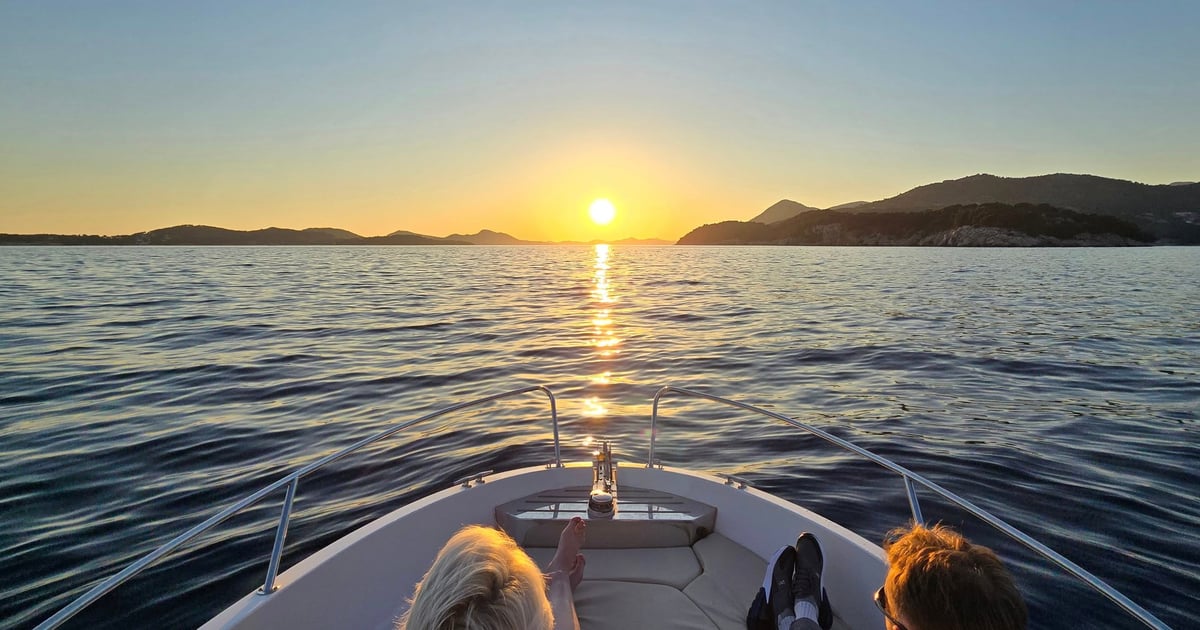 Two guests at the bow of a small boat watching the sun go down over the sea off Dubrovnik