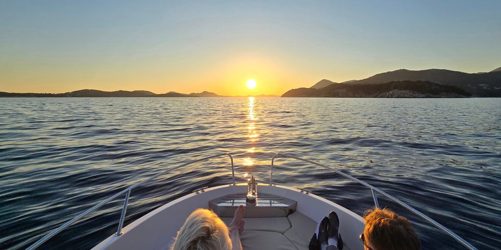 Two guests at the bow of a small boat watching the sun go down over the sea off Dubrovnik