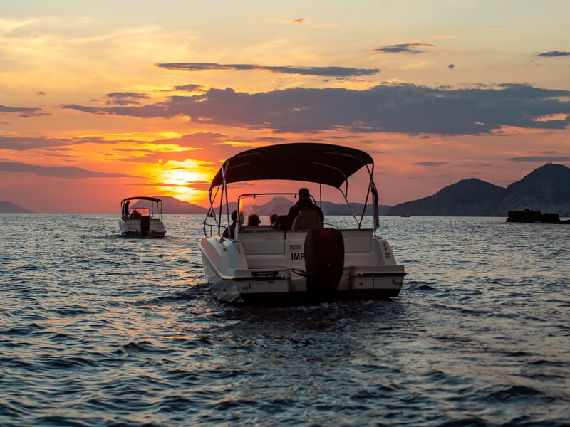 A canopy speedboat on calm water at sunset, with islands behind