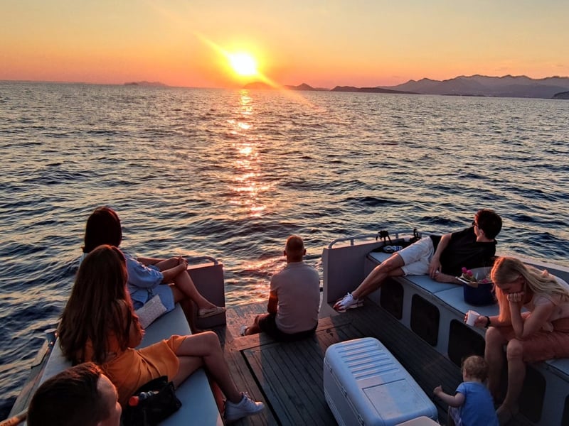 Guests relaxing on the deck of a boat as the sun sets over the sea