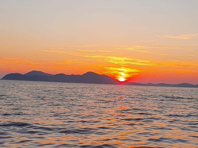 The sun setting behind a line of islands, seen from a moving boat off Dubrovnik